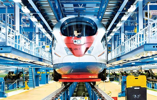 Modernt passagerartåg placerat i en produktionsanläggning, omgiven av industriell utrustning och teknisk infrastruktur – fokus på tillverkning och montering inom tågindustrin